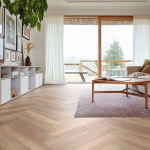 Living space with couch facing artwork wall, and cubbies, with light brown woodgrain LVP floors installed in herringbone design, with sliding glass doors leading to balcony