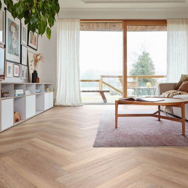 Living space with couch facing artwork wall, and cubbies, with light brown woodgrain LVP floors installed in herringbone design, with sliding glass doors leading to balcony