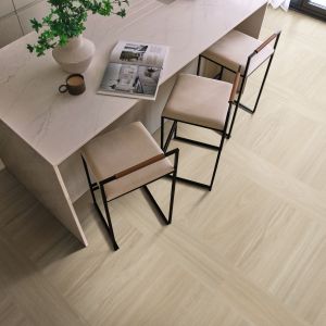 Overhead look at vase, coffee cup, and magazine spread atop a kitchen island, with barstools loosely tucked, over pale taupe woodgrain floor installed in a grid design
