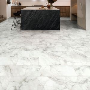 Minimalist kitchenette featuring wooden cabinets, large black stone island, stools, pendant lights, and white marble tile floor