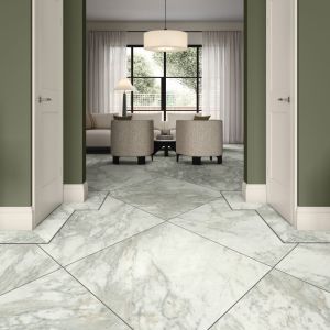 Passageway with large square marble tiles traced with a perimeter design border, flanked by two white doors, with view of armchairs, sofa, chandelier, and large window beyond