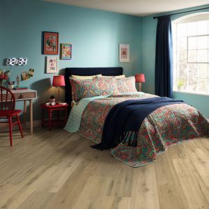 Teenager's bedroom with vibrant paisley bedding, nightstands, lamps, desks, and colorful hanging artwork, with wood plank flooring installed on a diagonal