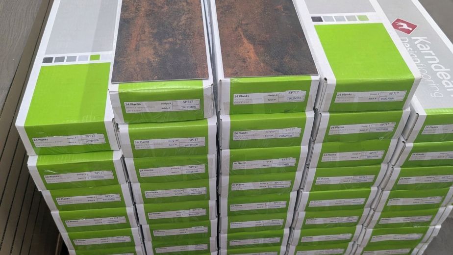 Pallet stacked with rectangular green and gray LVT cartons, with two Russus planks on top