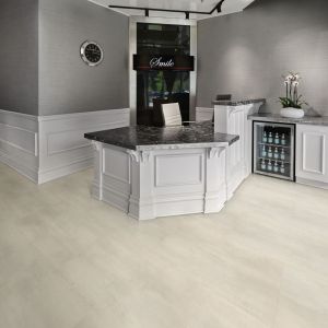 Healthcare space with "Smile" sign behind white and black reception desk and cabinetry with built-in mini fridge, over Stratus tile floor