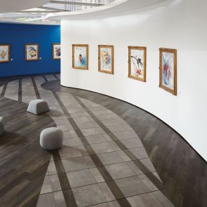 Architectural art gallery hall featuring multiple ottomans and gray tile path inlaid and surrounded by black planks