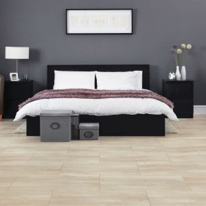 Simple monochromatic bedroom with hanging artwork, black furniture, and leather armchair, over taupe travertine flooring