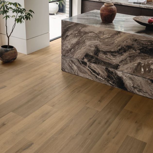 Mid brown reclaimed woodgrain plank flooring, houseplant, and corner of large stone kitchen island