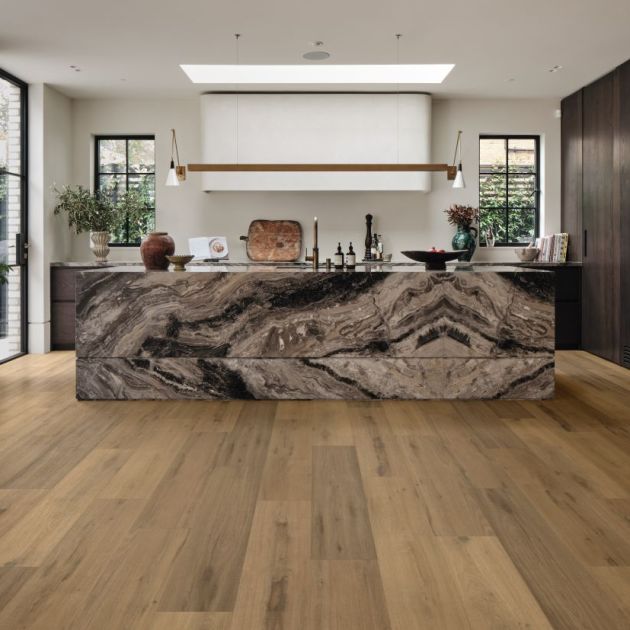 Kitchen featuring oversized black, bronze, and cream quartzite island, reclaimed wood floor, and walnut cabinetry