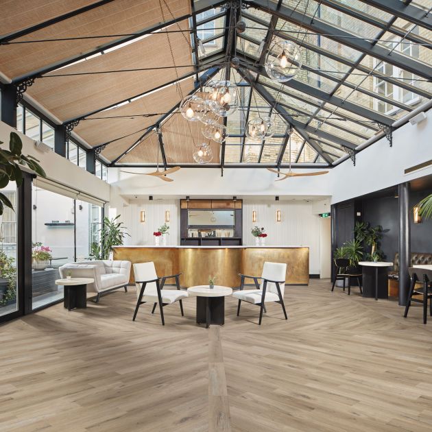 Commercial space featuring domed skylights, brushed gold counter, and various chairs and couches dispersed across beige woodgrain floor installed in a pattern