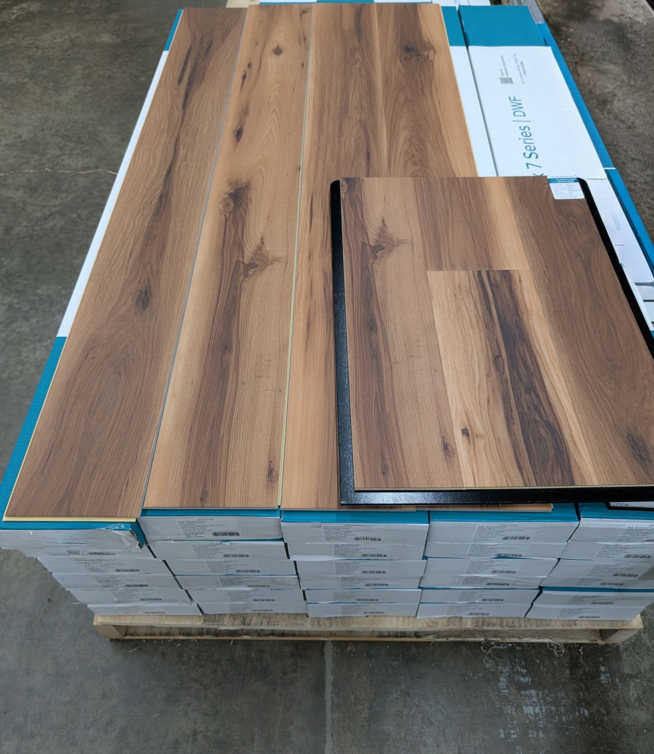 Pallet of teal and white cartons of LVP flooring with Smoked Amber planks and sample on top